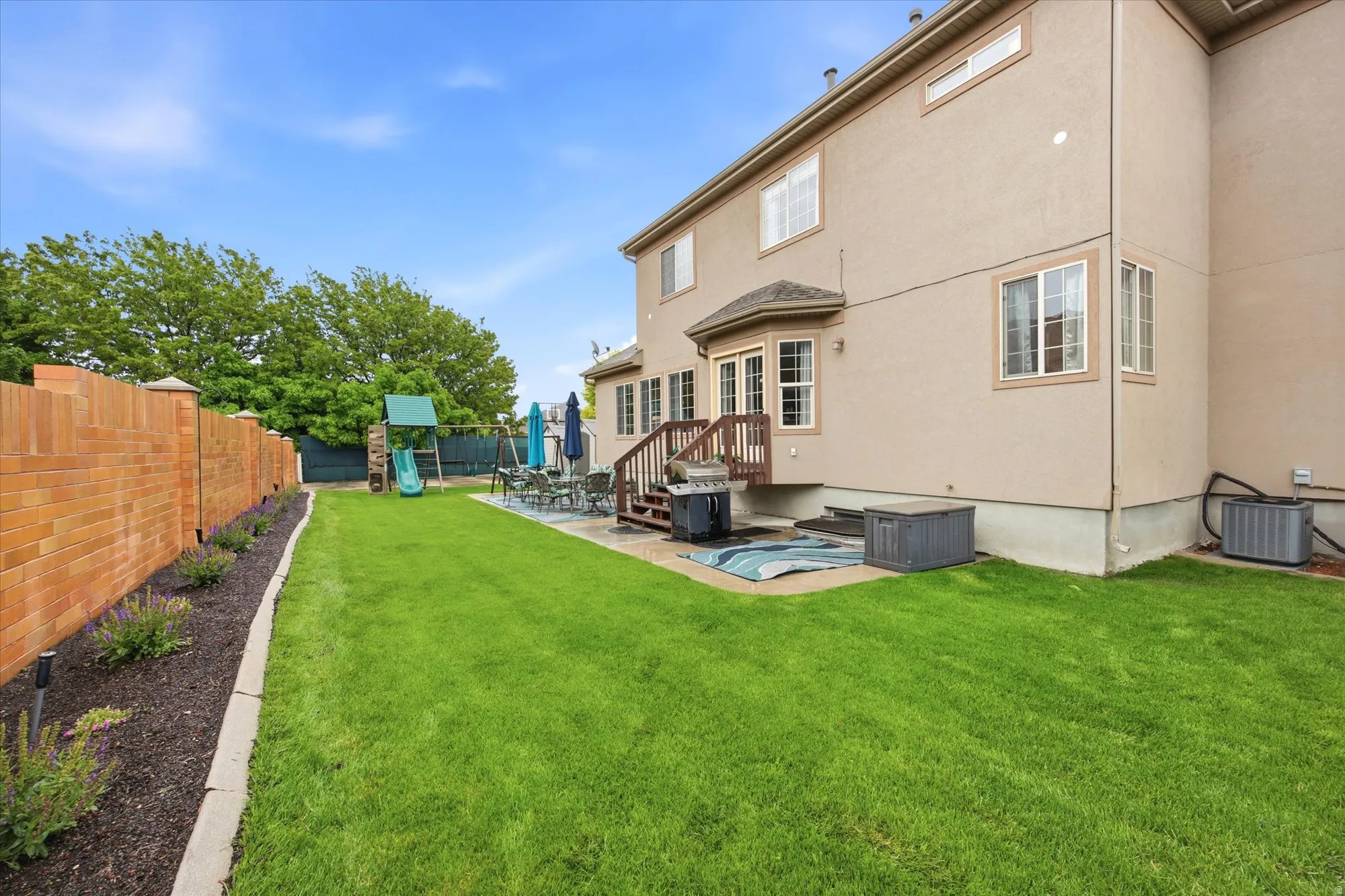 Expansive backyard featuring a manicured lawn, a full-height brick privacy fence, and a patio area with direct access to the interior