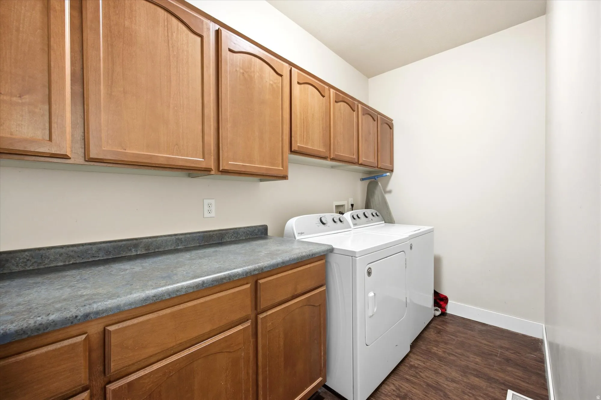 Dedicated laundry area with wood-finish flooring, extensive wood cabinetry, and a durable countertop