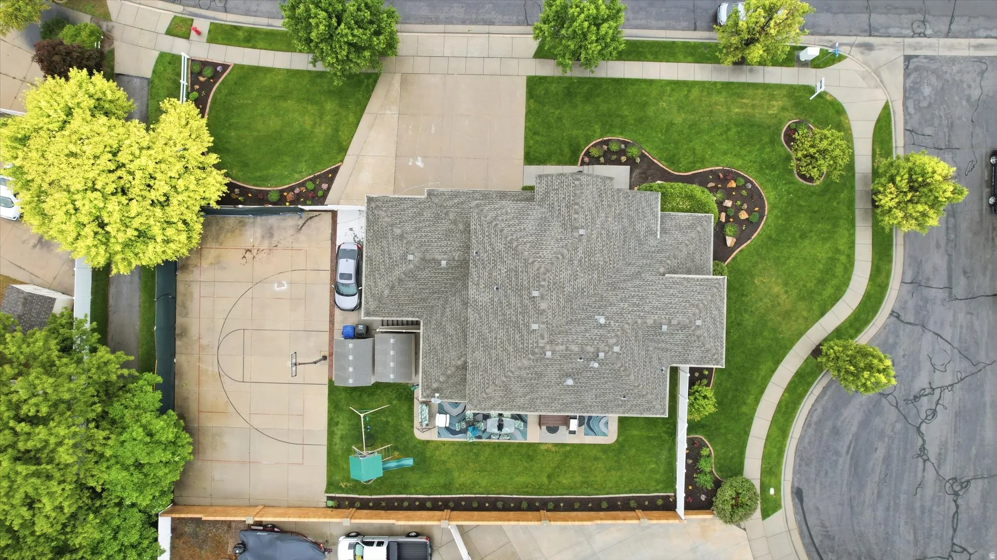 Expansive property featuring a multi-gabled roofline, concrete driveway, and a paved sport court