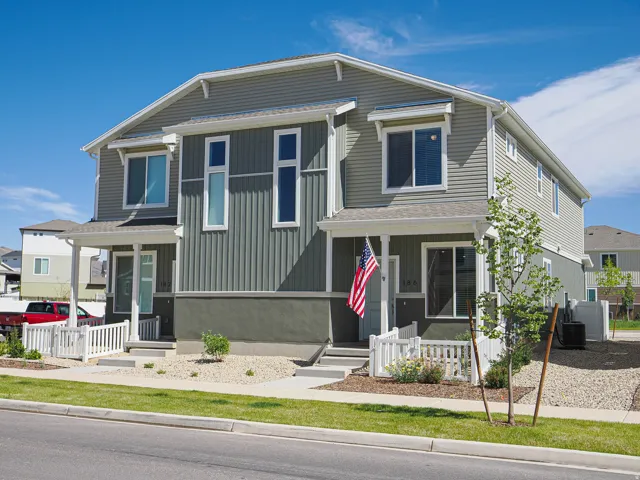 Modern townhome exterior featuring light gray siding with vertical accent panels, white window trim, a covered entry porch, and a white picket fence