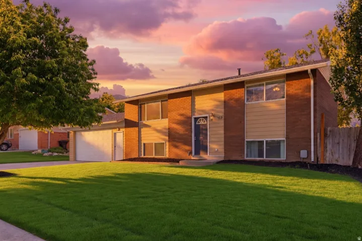 Split-level exterior featuring brick and horizontal siding, a two-car garage, and a manicured front lawn