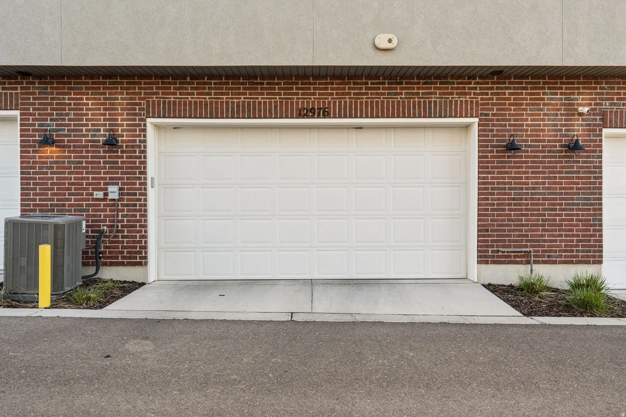 Brick exterior with a white panel garage door, concrete driveway, and black wall sconces