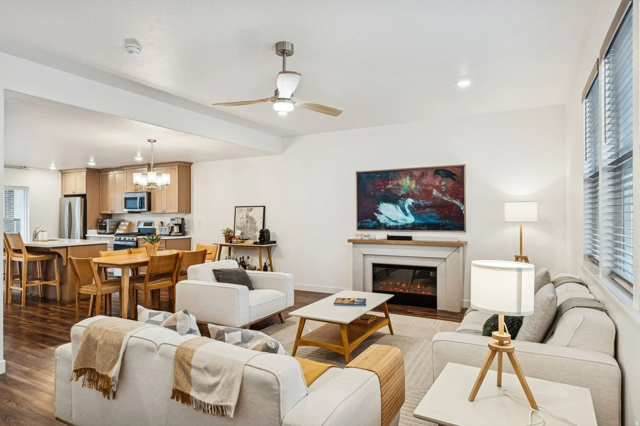 Open-concept living space featuring wood-finish flooring, a contemporary ceiling fan, and an electric fireplace with mantel