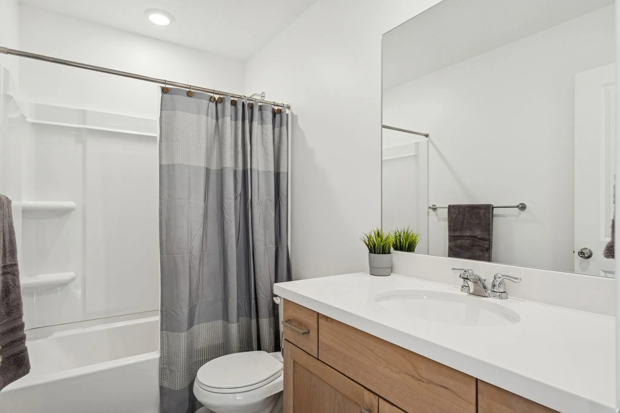 White bathroom featuring a single-sink vanity with wood-finish cabinetry, a white countertop, and a large wall-mounted mirror