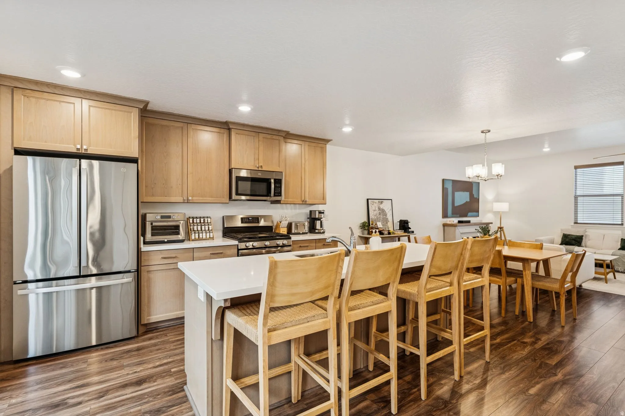 Open-concept kitchen and living area featuring wood-finish flooring, light-toned cabinetry, stainless steel appliances, a white island with seating, and recessed lighting