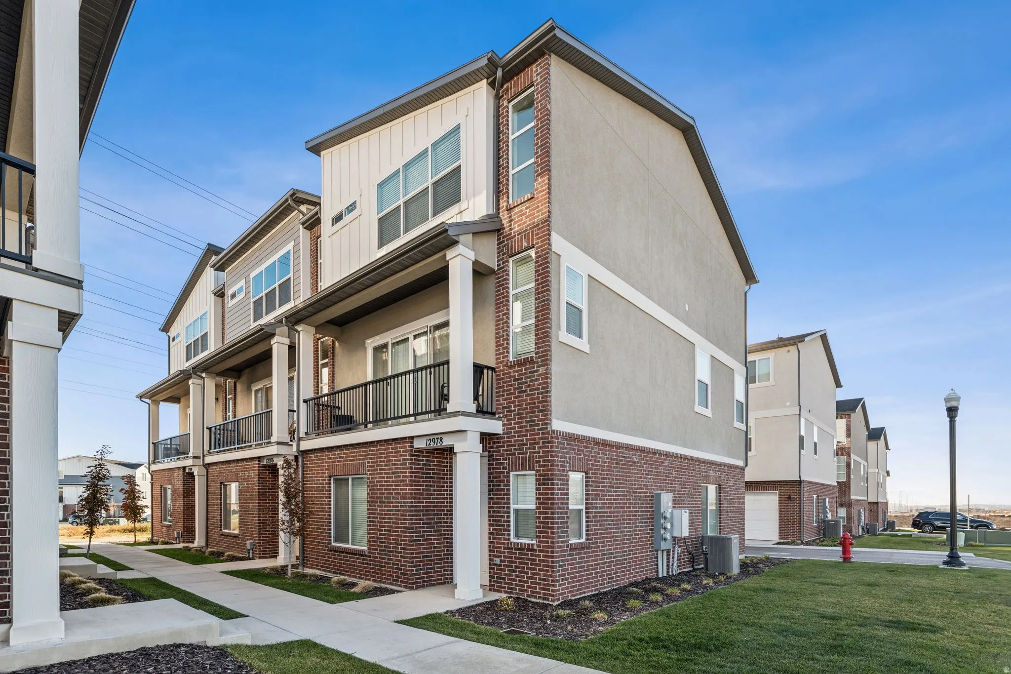 Modern townhouse exterior featuring brick and siding accents, multiple windows, a private balcony with black railings, and an individual unit entrance