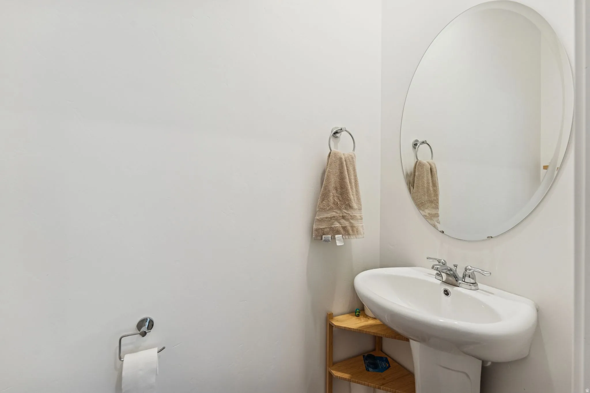 Pedestal sink with chrome faucet, complemented by an oval wall mirror