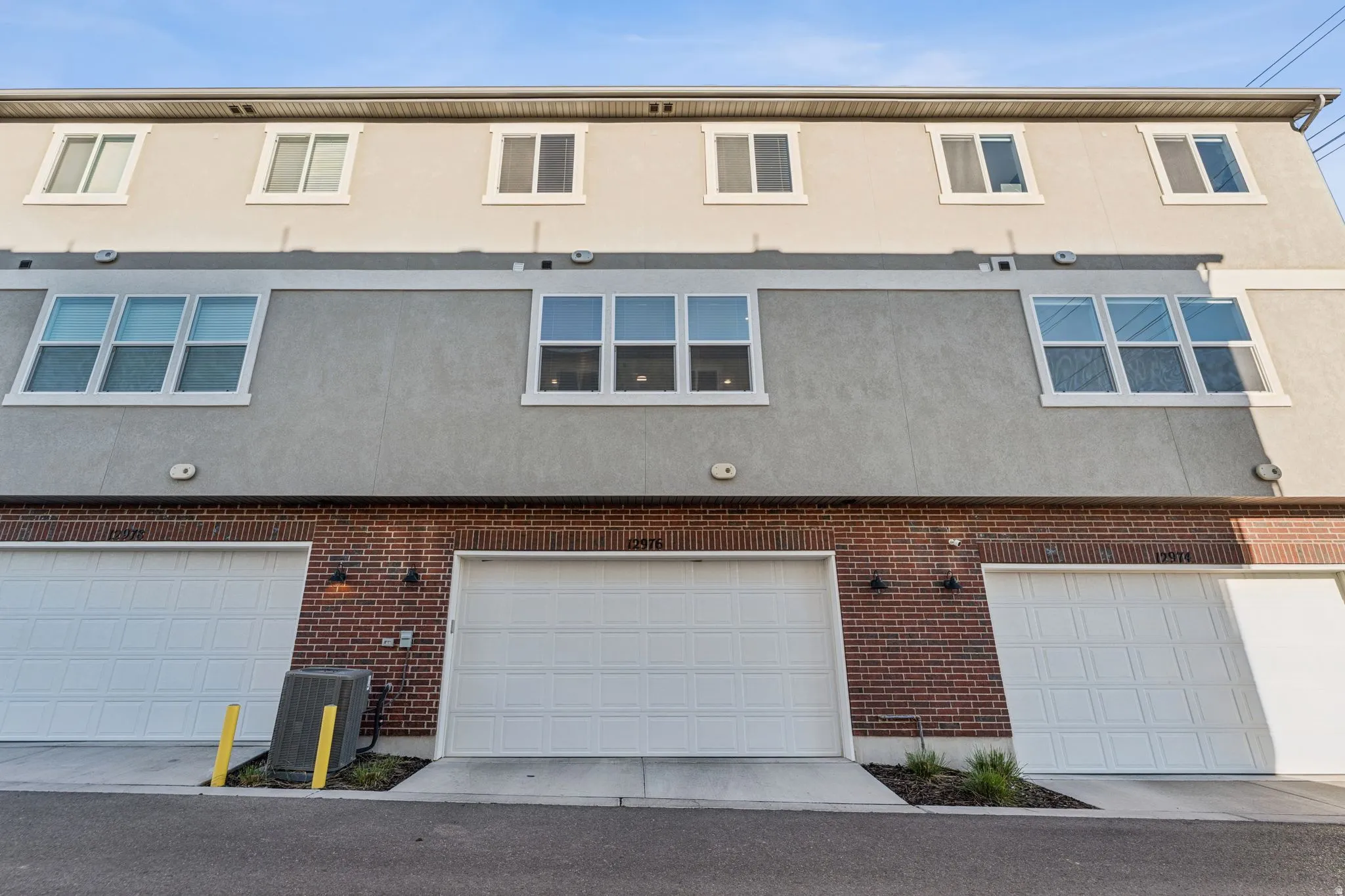Contemporary exterior featuring a stucco facade, brick accents, multiple windows, and three white garage doors