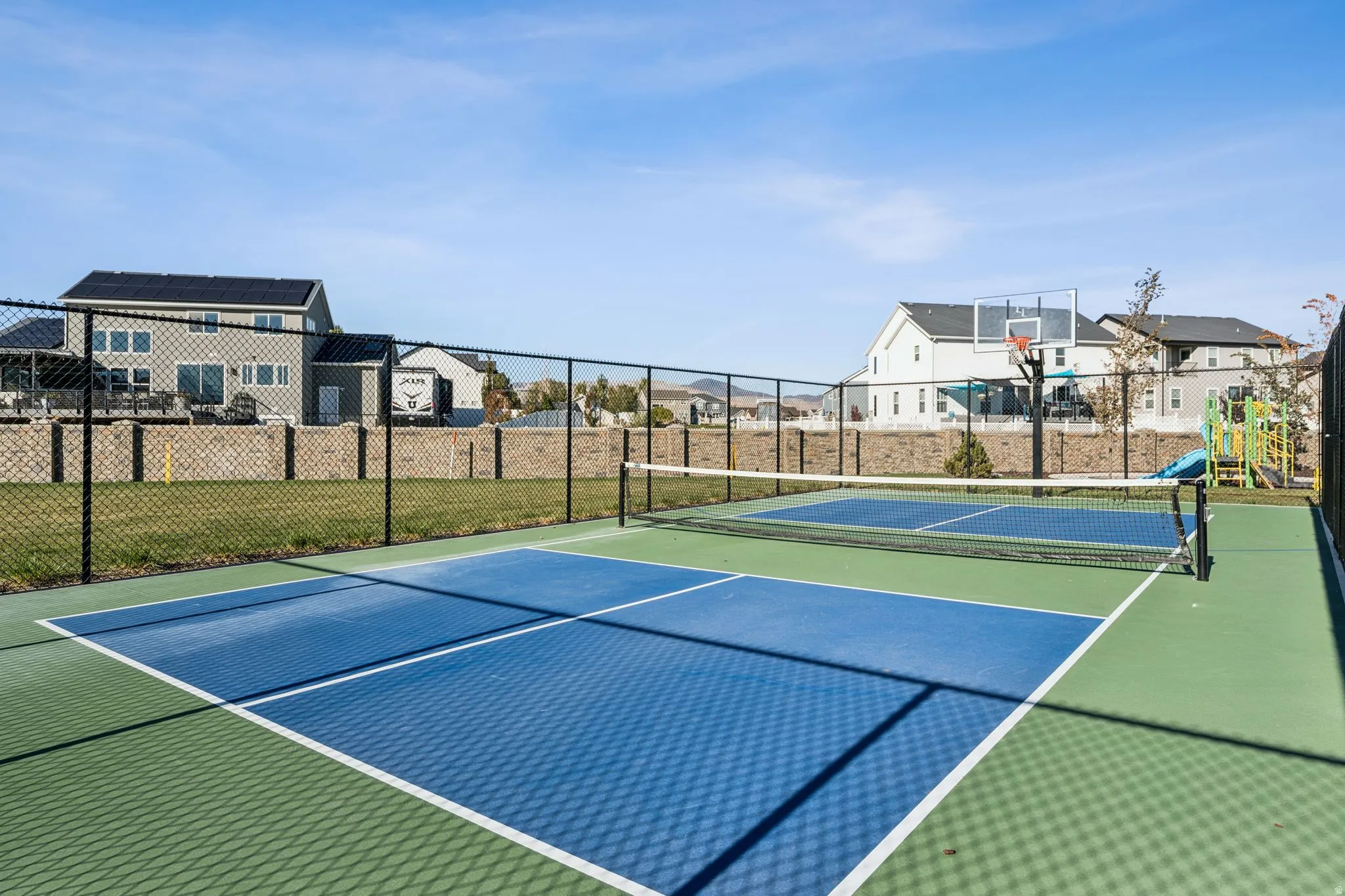 Fenced sports court featuring two blue and green pickleball courts with white line markings