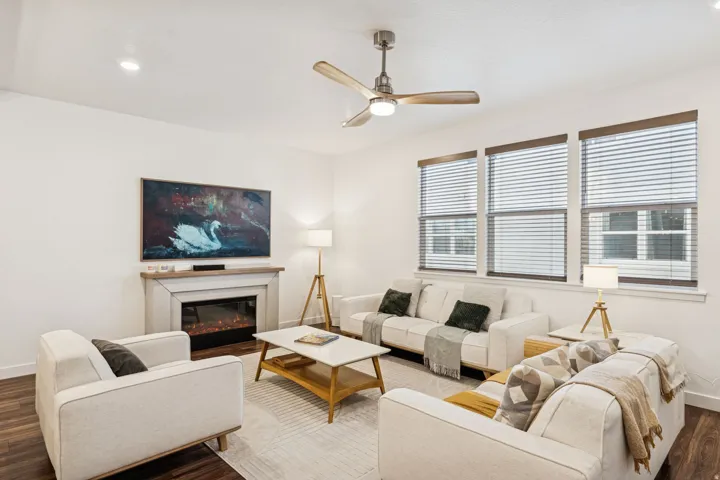 Living area featuring wood-finish flooring, a contemporary fireplace with a light-toned mantel, recessed lighting, and multiple windows with blinds