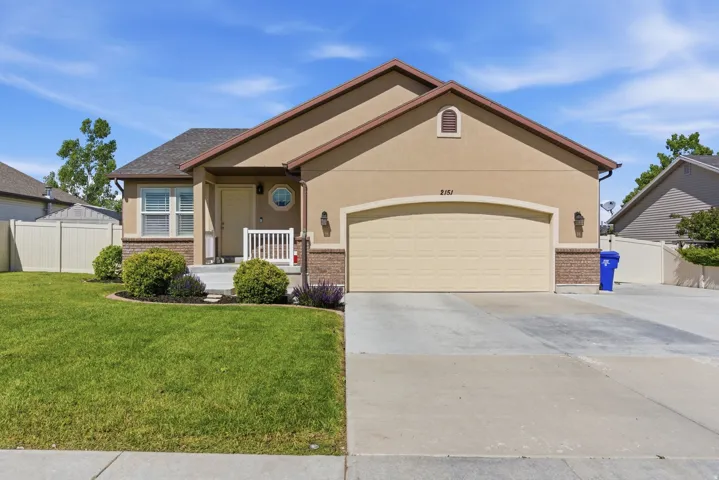 Exterior featuring a stucco facade with brick accents, a gabled roofline, an attached garage, a concrete driveway, and a front porch with white railing