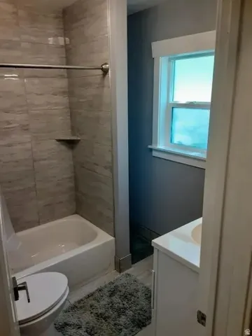 Bathroom featuring a white bathtub with subway tile surround, a built-in shower niche, a window with white trim, and a vanity with a white countertop and integrated sink
