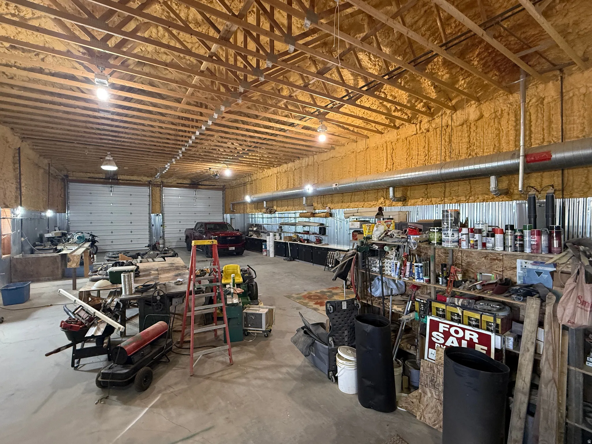 Spacious interior workshop featuring two large overhead doors, exposed wood truss ceiling, spray foam insulation, and corrugated metal wall panels
