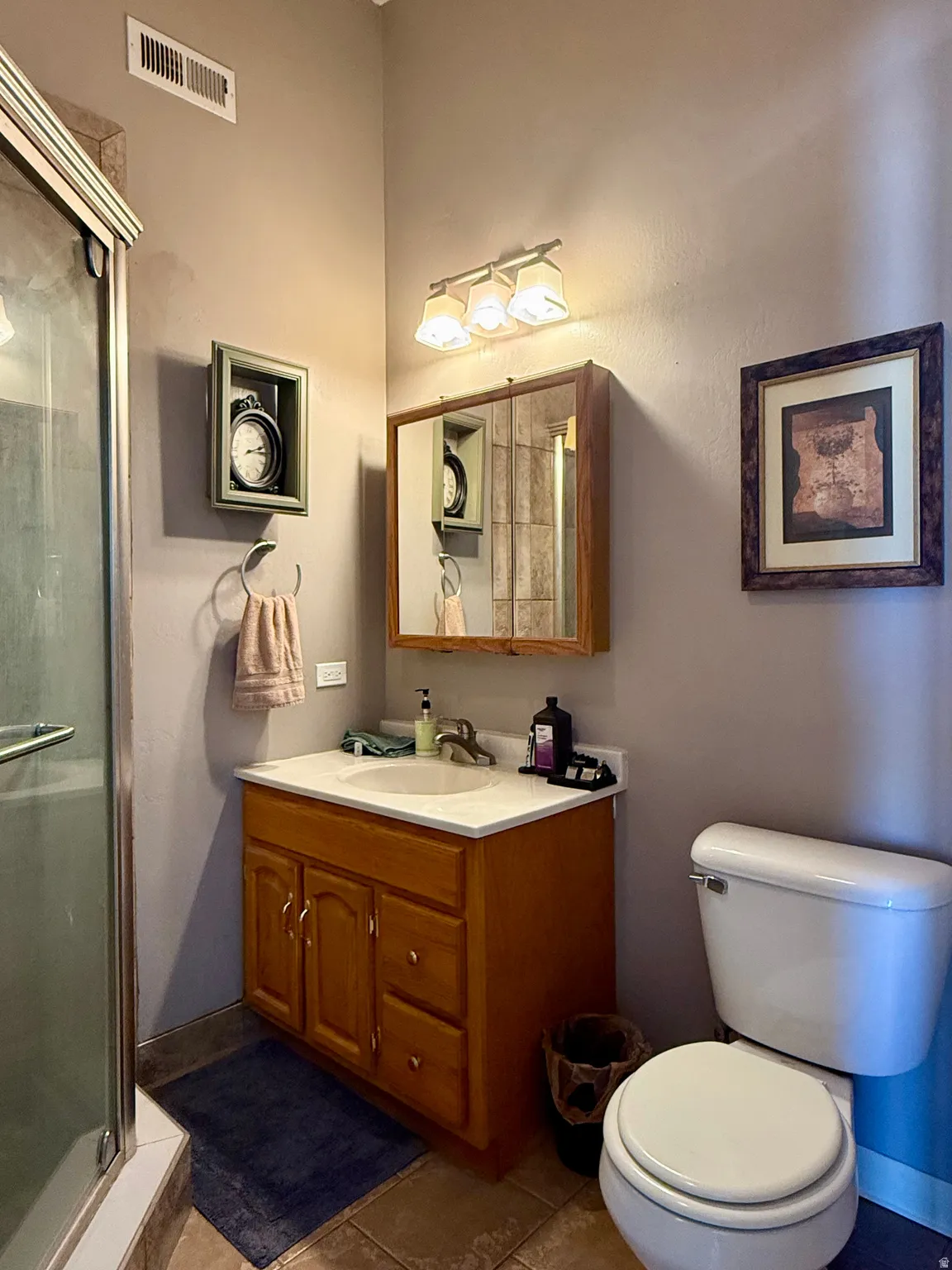 Bathroom featuring a wood-finish vanity with an integrated sink and light-toned countertop, a frameless glass shower enclosure, and ceramic floor tiling