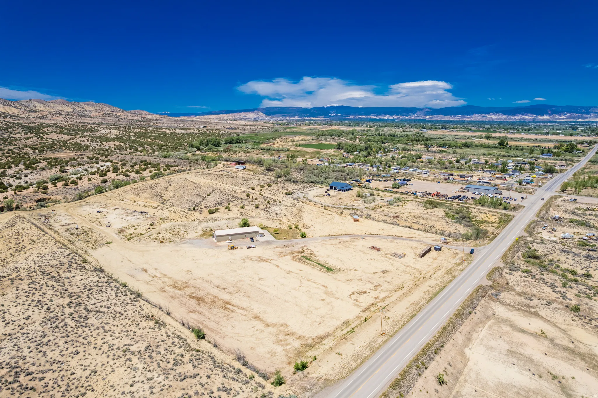 Expansive undeveloped land featuring a long road frontage, a distant mountain range, and scattered vegetation