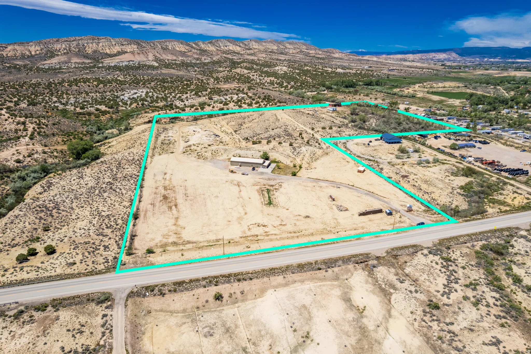 Expansive undeveloped land featuring a single-story structure, direct road frontage, natural topography, and distant mountain backdrops