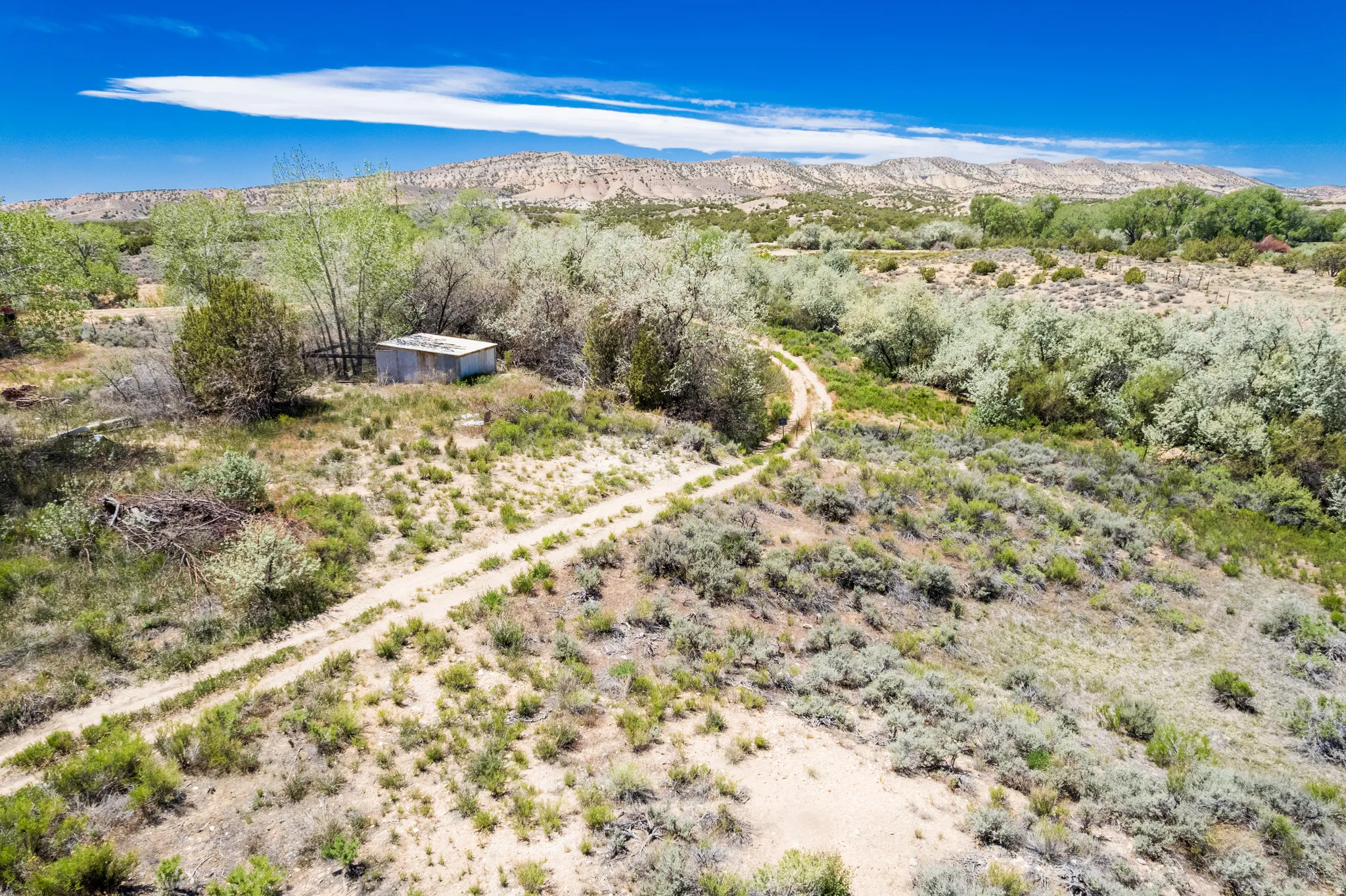 Expansive property featuring a winding dirt path, diverse vegetation, and distant natural landforms