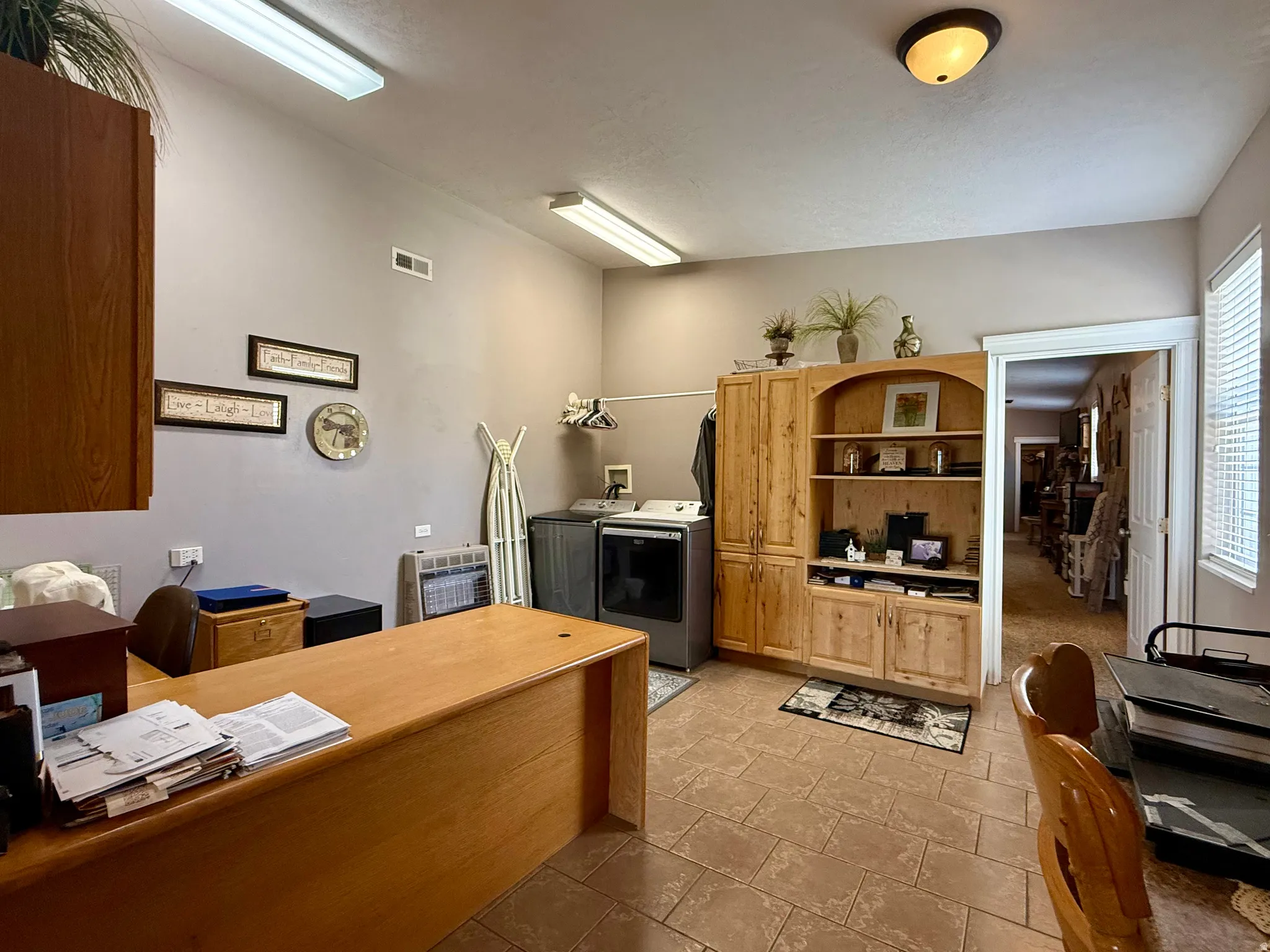 Utility space featuring tiled flooring, built-in wooden cabinetry, recessed fluorescent lighting, a window with blinds, and a neutral wall color