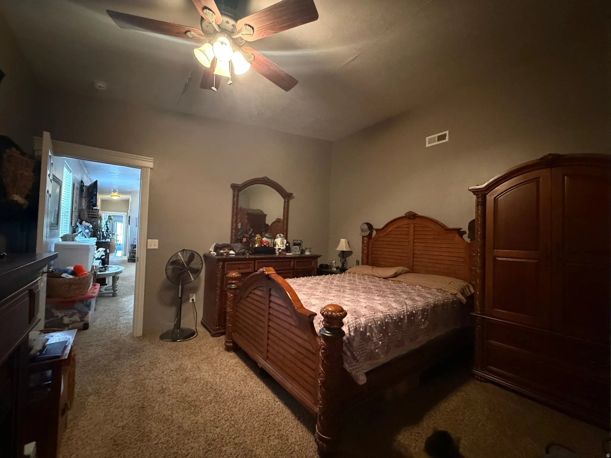 Carpeted room featuring a ceiling fan with integrated lighting, a wall vent, and a doorway opening to another interior space