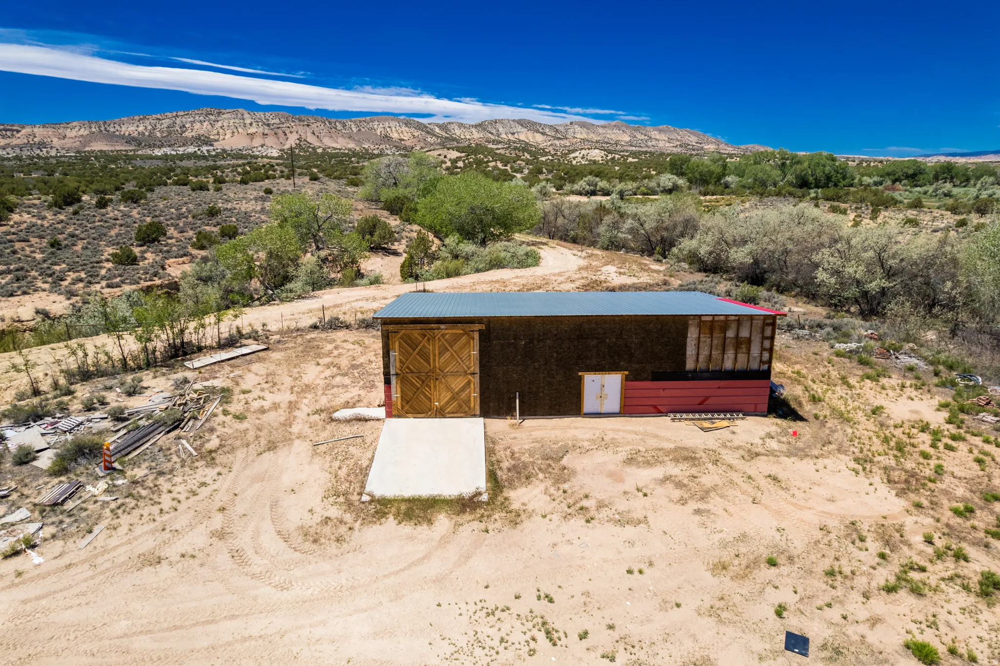 Barn structure with a metal roof, featuring a large wooden sliding door, red lower siding, and a concrete slab entrance