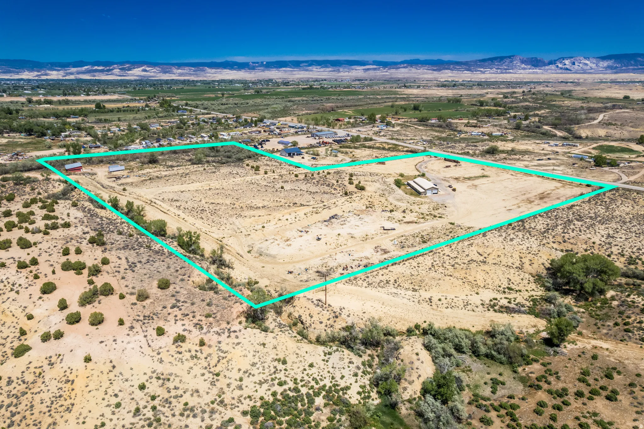 Expansive land parcel featuring multiple structures, including a primary residence and outbuildings, with a gravel driveway