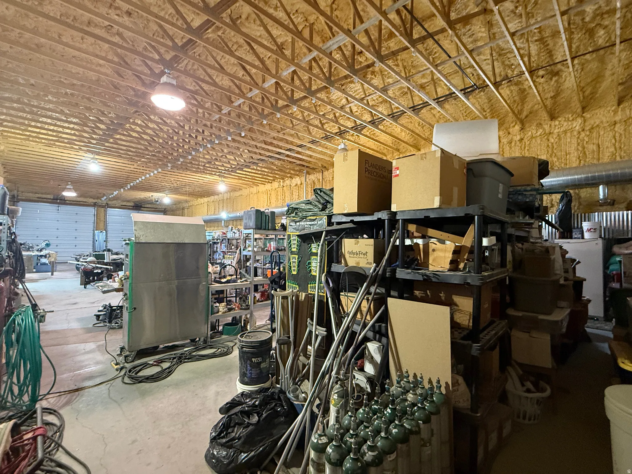 Spacious interior featuring exposed wood truss ceiling, spray foam insulation, and multiple high-bay light fixtures