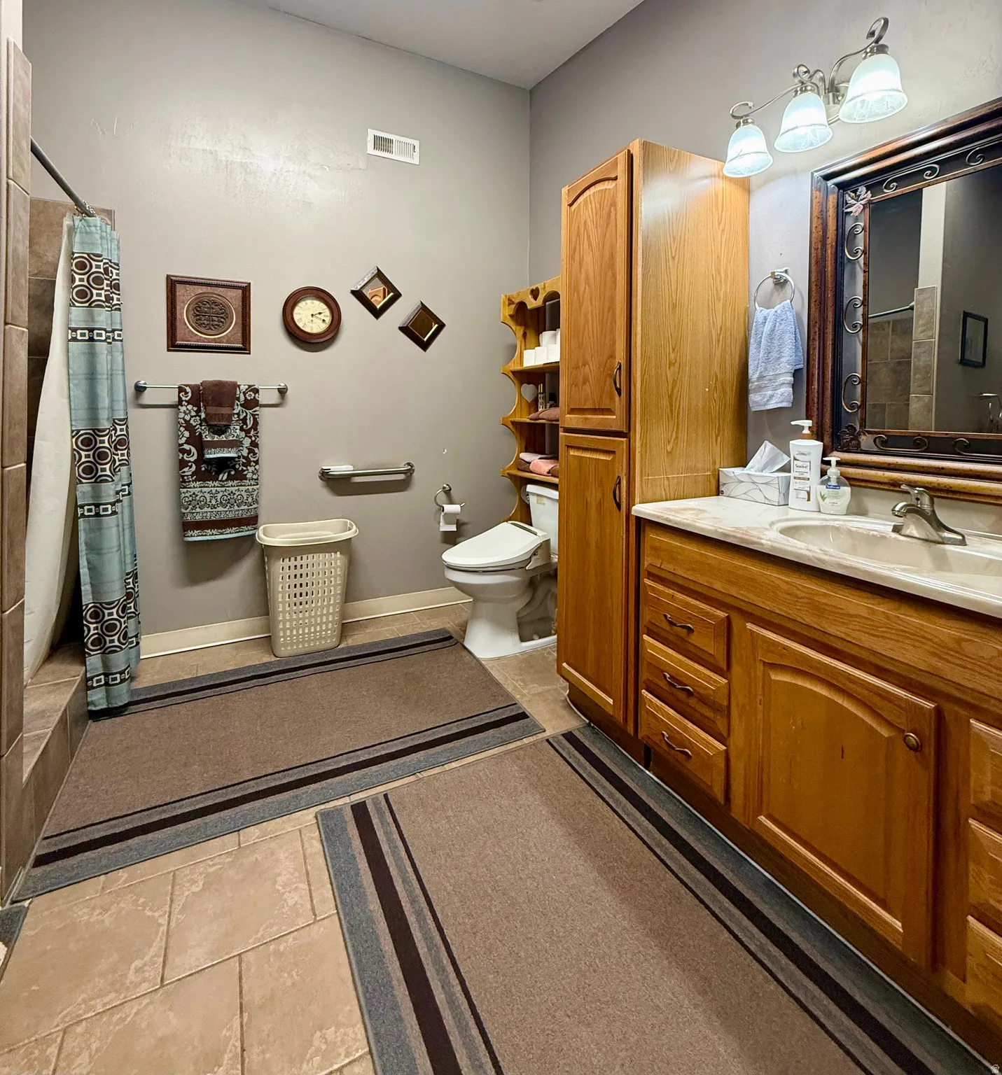 Bathroom featuring a vanity with a cultured marble countertop, an ornate framed mirror, a three-light fixture, and wood-finish cabinetry