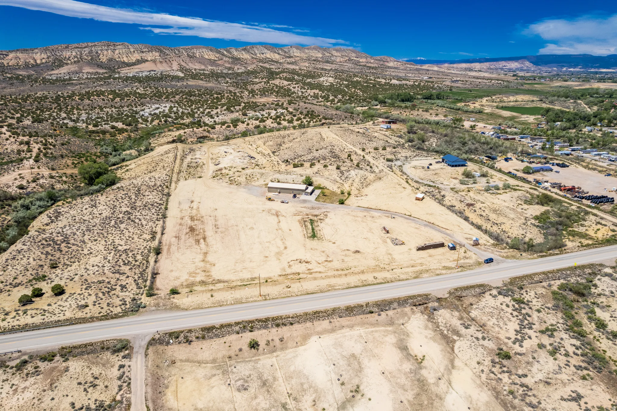 Expansive land parcel featuring a single-story structure, direct road frontage, and a surrounding natural landscape with distant mountains