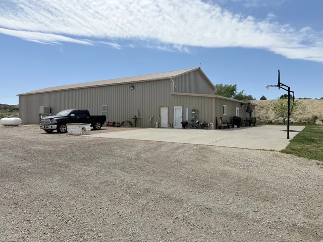 Expansive metal-sided building featuring a large concrete pad, gravel driveway, and a basketball hoop