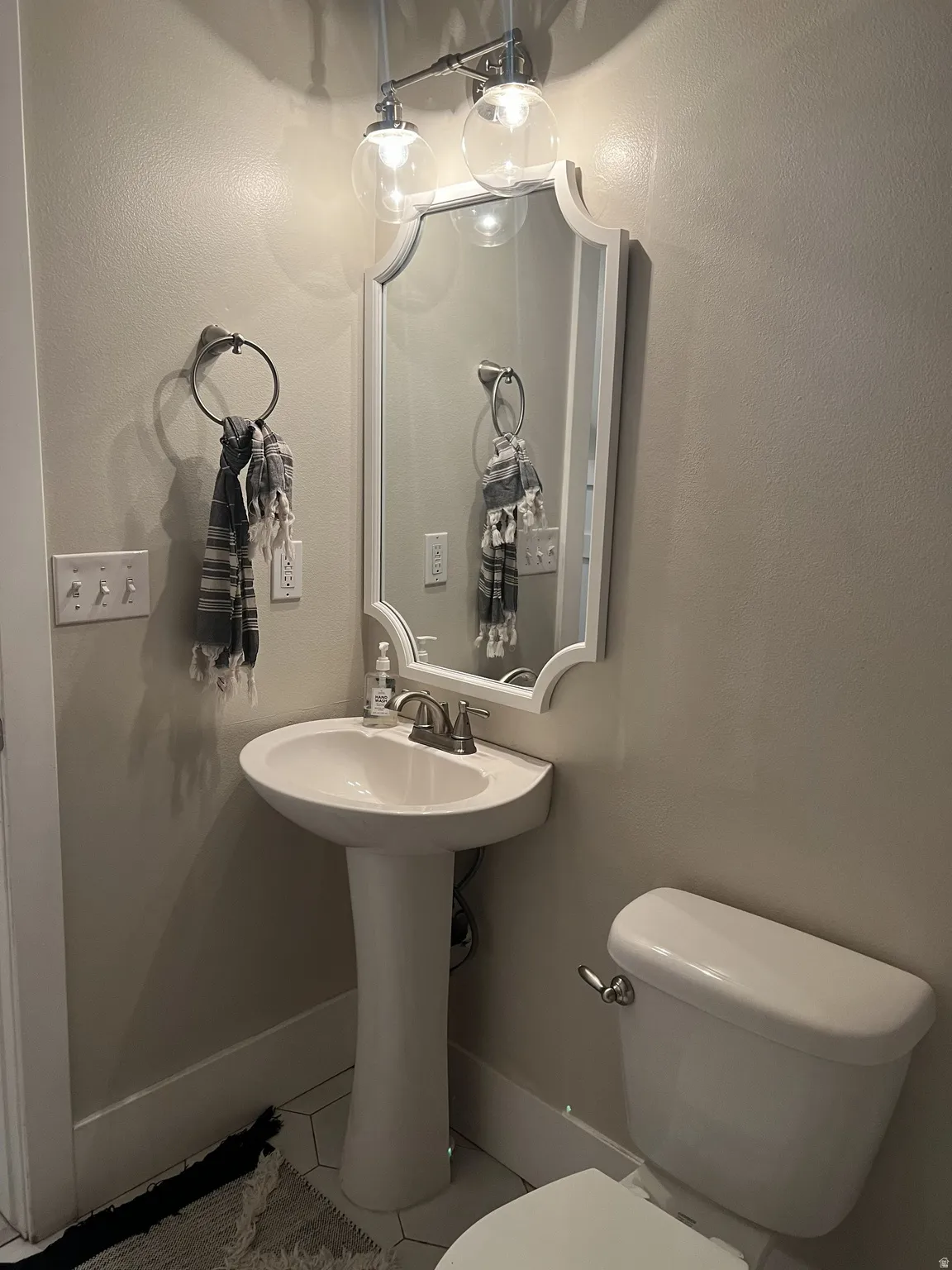 Pedestal sink with chrome faucet, complemented by a decorative mirror and two-light vanity fixture