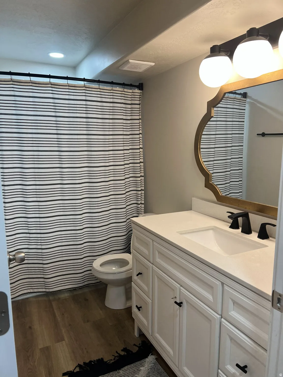 Contemporary bathroom featuring a white vanity with integrated sink, black fixtures, and a decorative gold-framed mirror