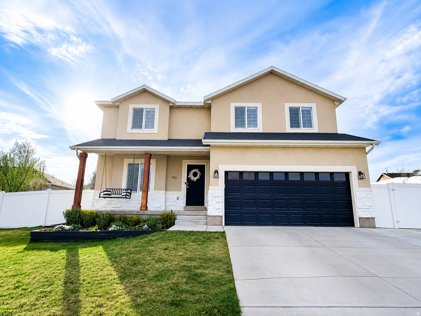 Two-story stucco residence featuring a covered front porch with wood-wrapped columns, a dark entry door, and a white fence