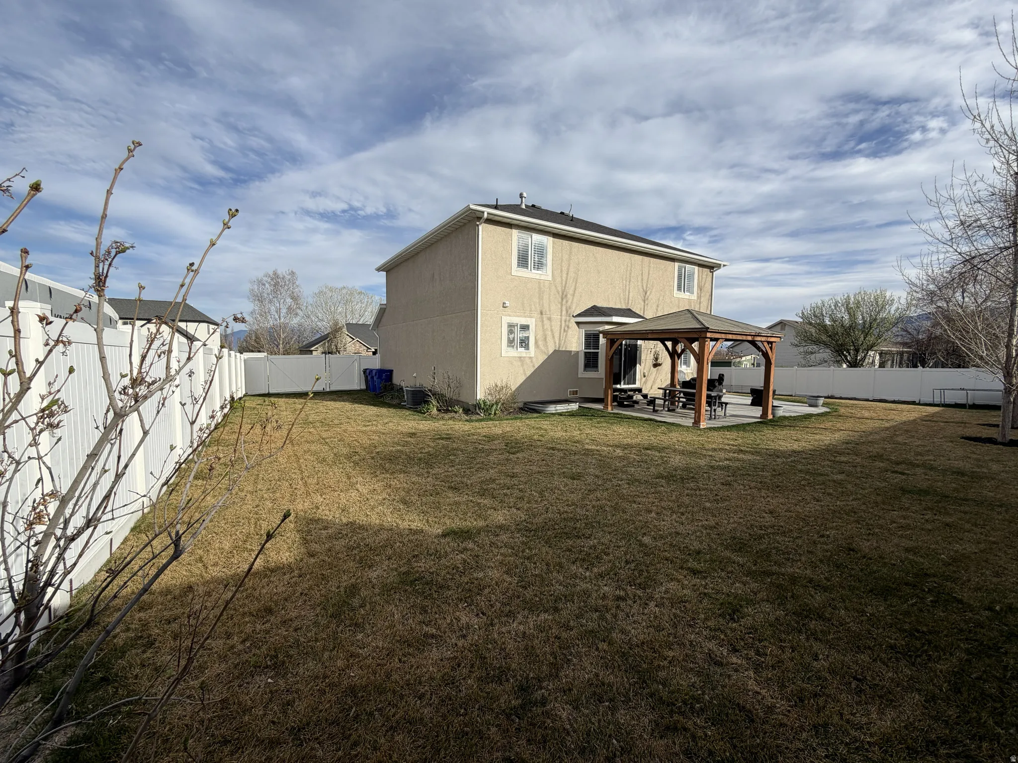Expansive backyard featuring a gazebo-covered patio, mature trees, and a full perimeter fence