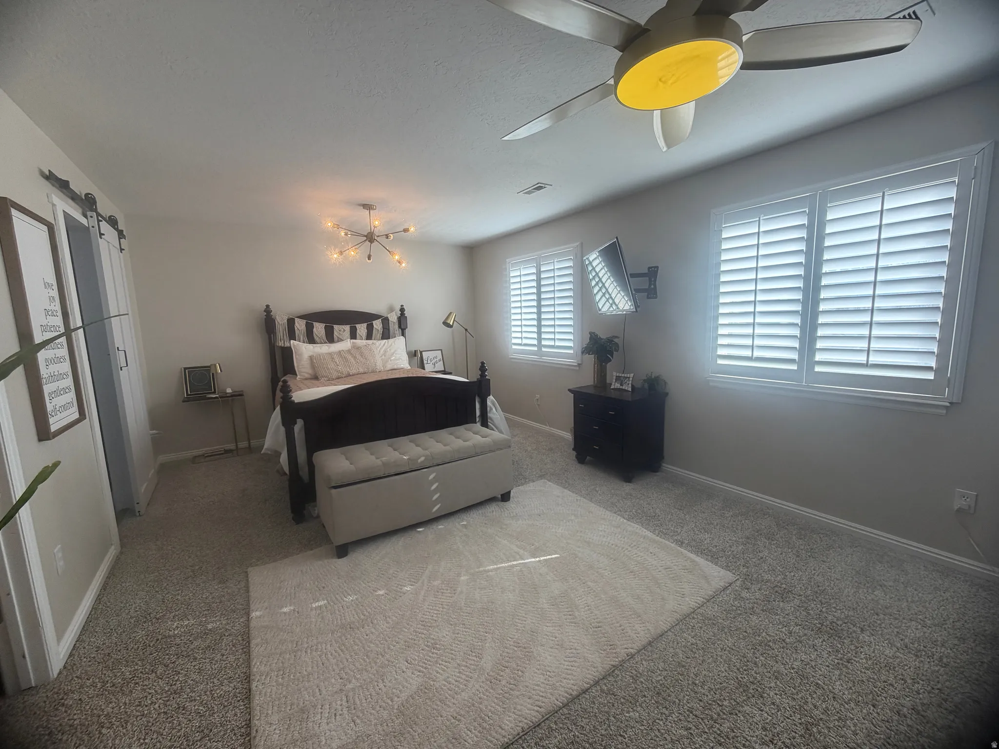 Spacious carpeted room featuring multiple windows with louvered shutters, a ceiling fan with integrated lighting, and a modern Sputnik-style chandelier