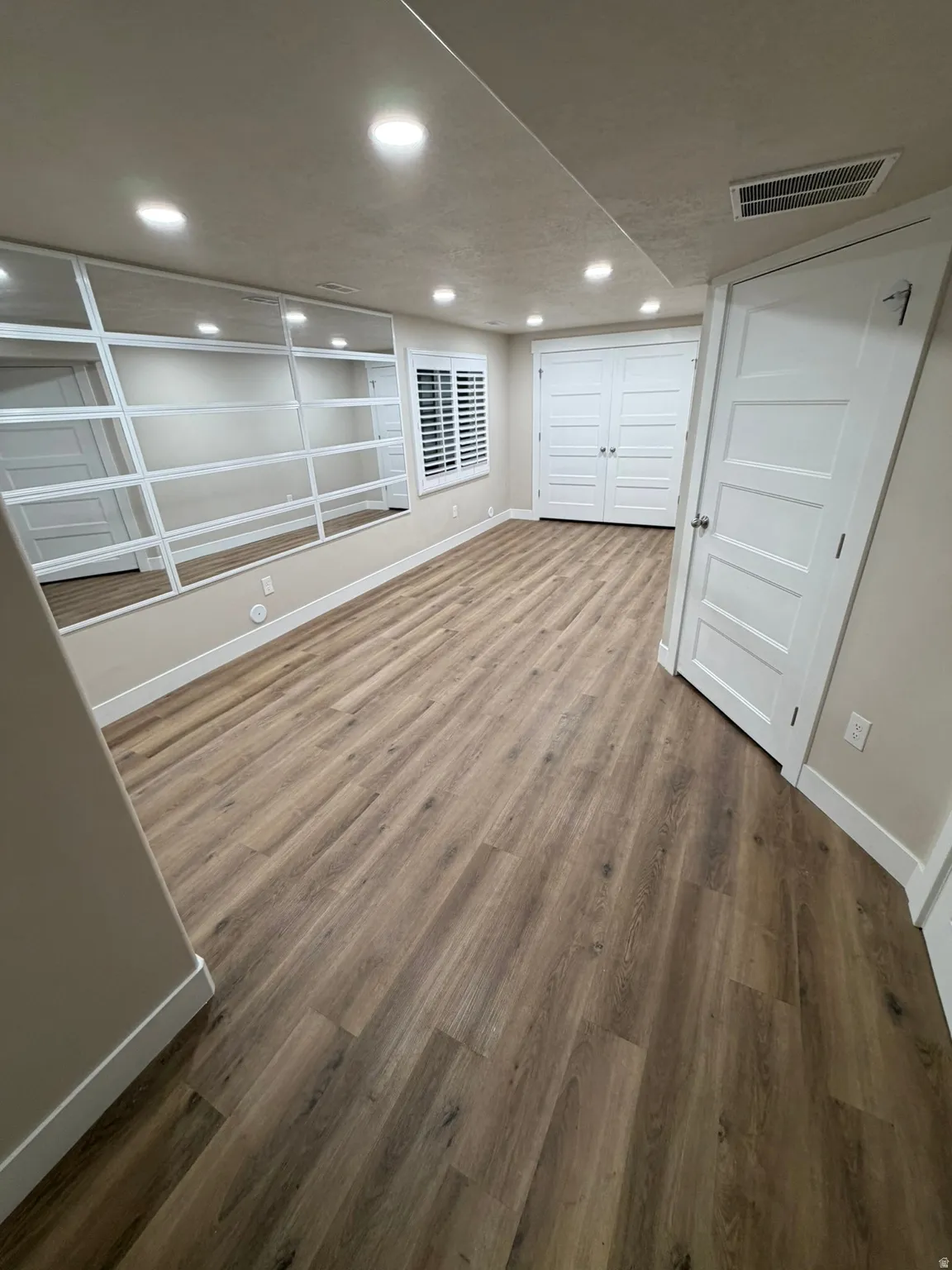 Spacious room featuring wood-finish flooring, recessed lighting, and a large mirrored wall with white framing