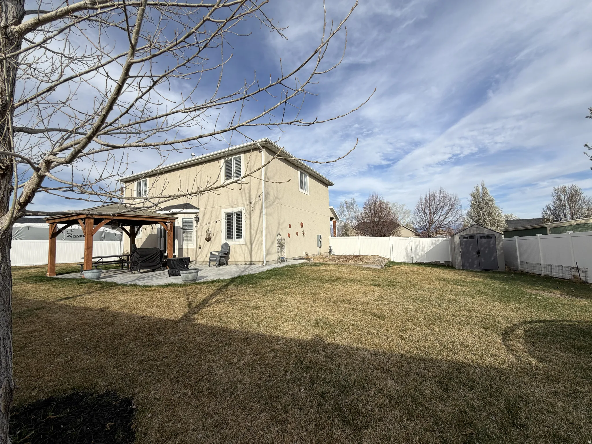 Expansive backyard featuring a concrete patio, a built-in wooden gazebo, a storage shed, and a full privacy fence