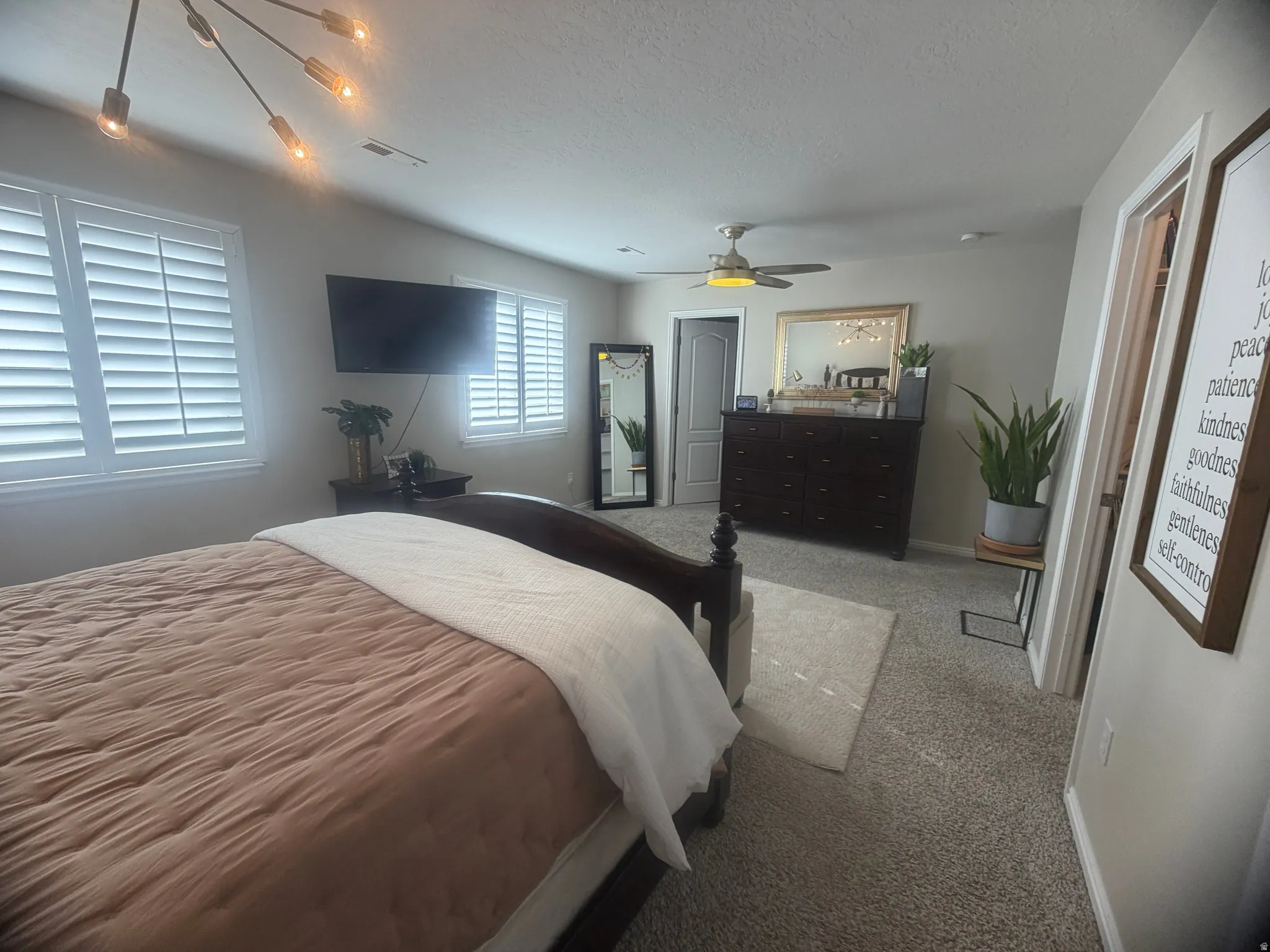 Spacious bedroom featuring multiple windows with white plantation shutters, neutral-toned carpeting, and a ceiling fan with integrated lighting