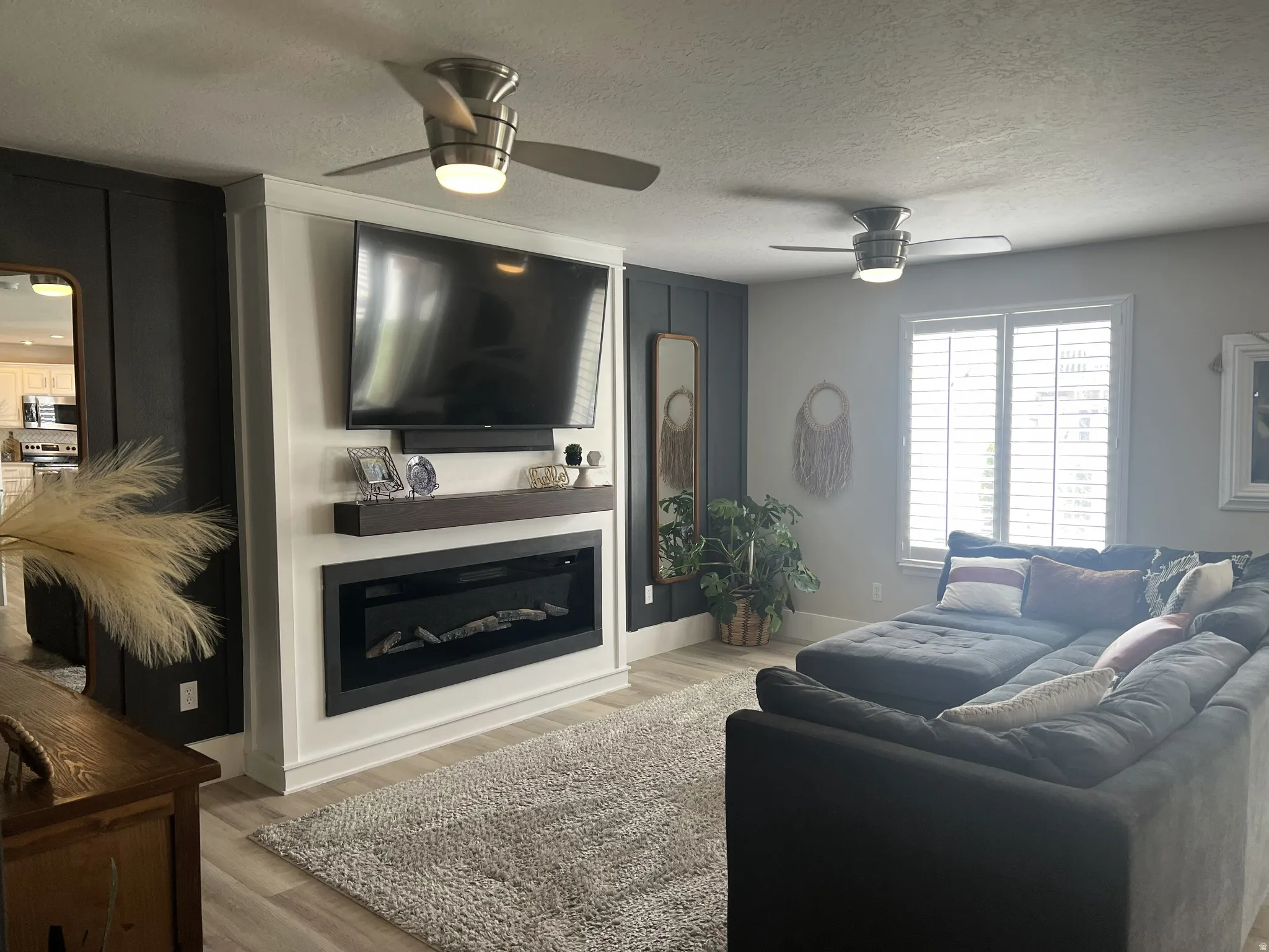 Living area featuring an electric fireplace with a wood-finish mantel, mounted television, and two ceiling fans with integrated lighting