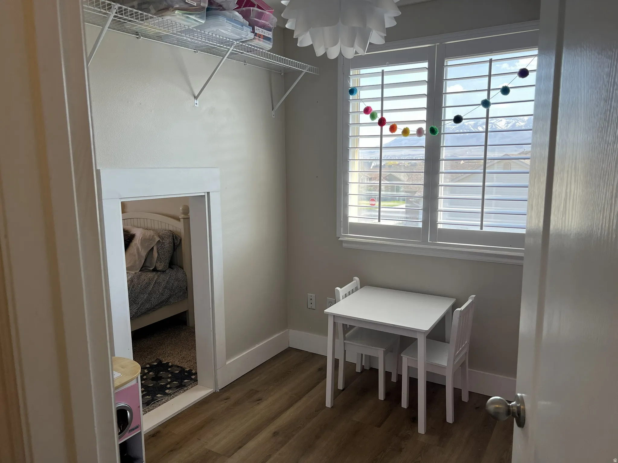 Windowed room featuring wood-finish flooring, white plantation shutters, and a built-in wire shelf
