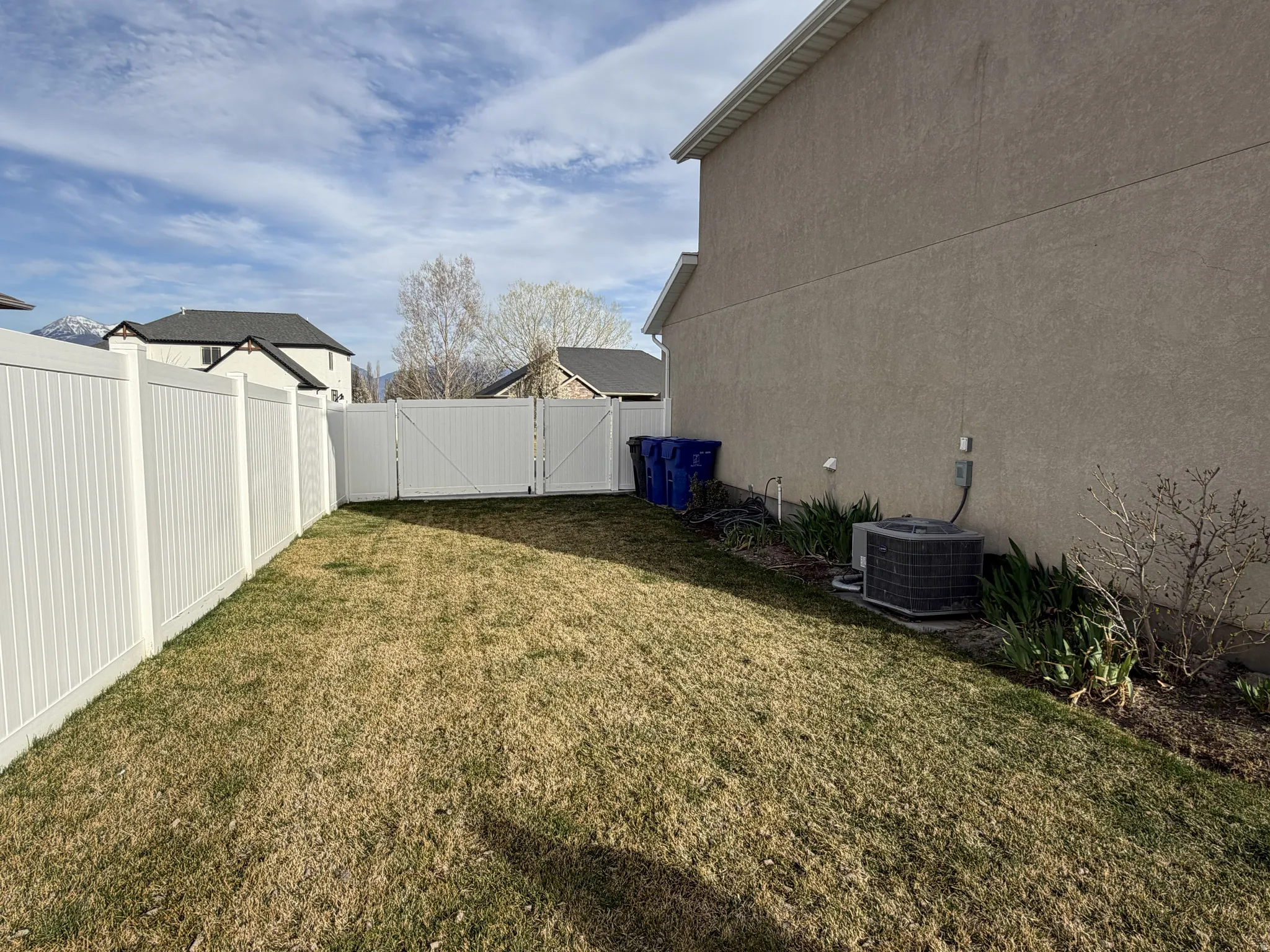 Fenced backyard featuring a white privacy fence, double gate access, and a stucco exterior