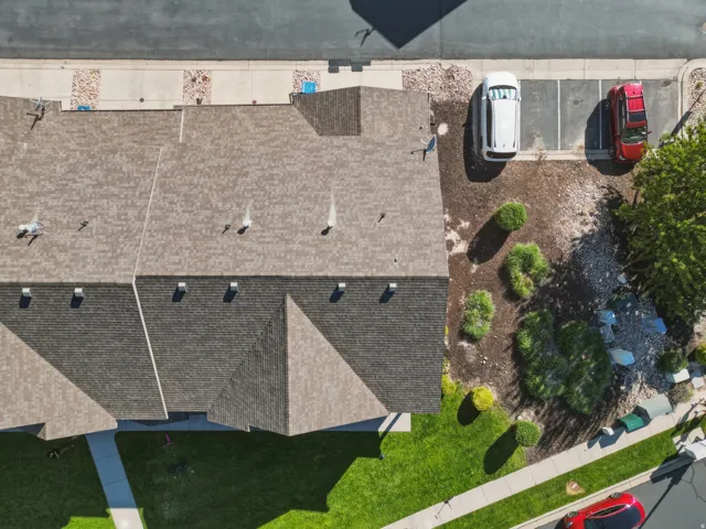 Shingle roofing with multiple vents, a paved two-car parking area, and a rock and shrub landscaped section