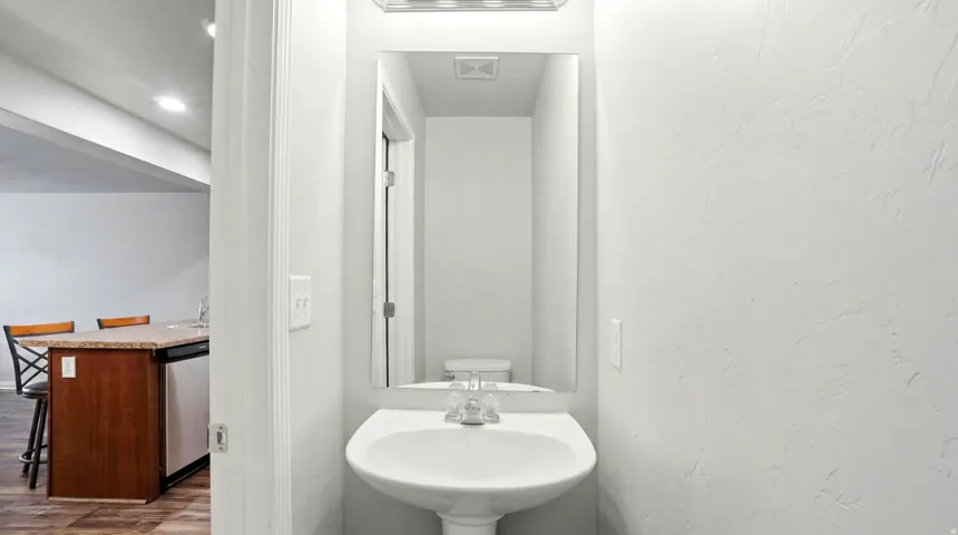 Pedestal sink with chrome fixtures and a vanity mirror, complemented by a contemporary light fixture