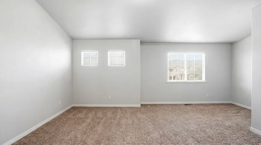 Spacious room featuring neutral carpeting, light gray wall paint, and white baseboards