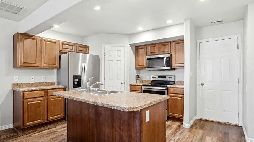 Kitchen featuring a center island with a double basin stainless steel sink, wood-finish flooring, recessed lighting, stainless steel appliances, and wood cabinetry with stone-look countertops