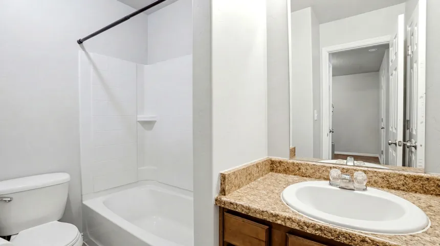 Bathroom featuring a white bathtub and shower surround, a white toilet, a vanity with a built-in sink, and a speckled countertop