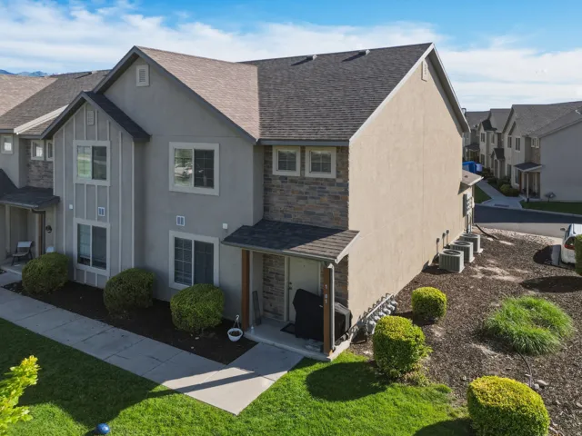 Multi-level townhome featuring a neutral stucco and stone facade, gabled roof, and multiple windows