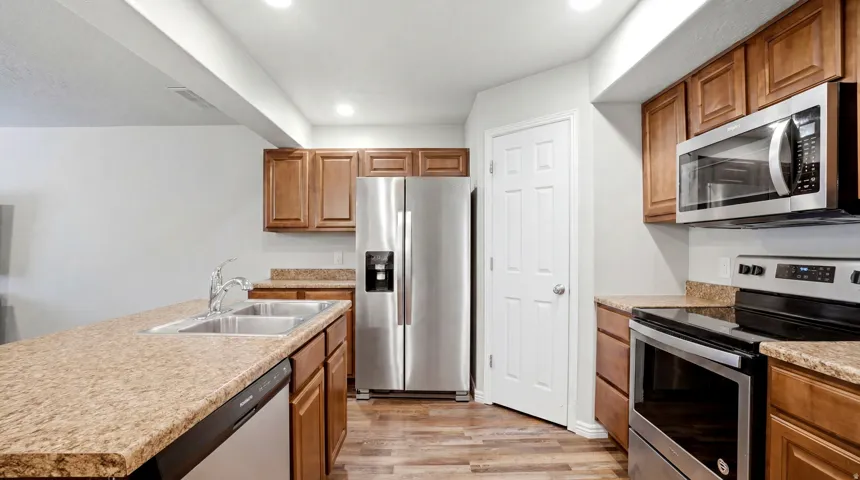 Kitchen featuring wood-finish flooring, recessed lighting, wood cabinetry, stainless steel appliances, and a double-basin sink