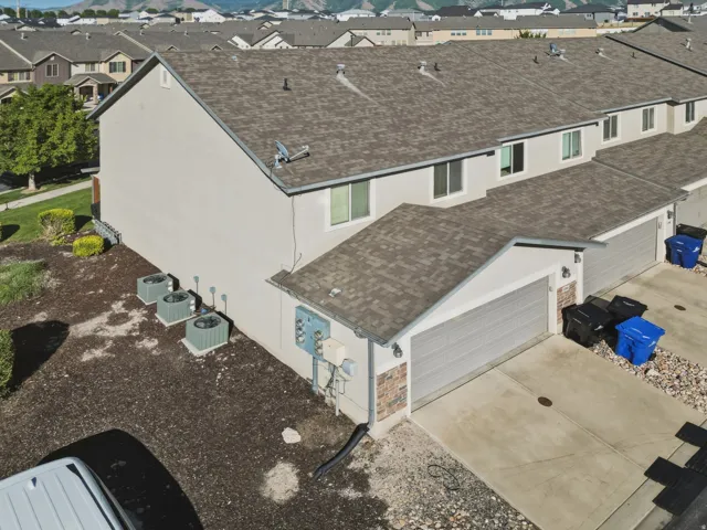 Contemporary townhome featuring a stucco and brick facade, an attached garage, paved driveway, and multiple HVAC units