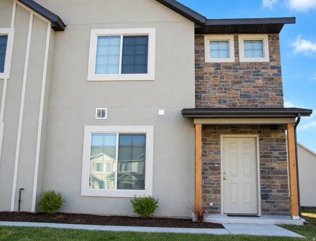 Stone and stucco exterior featuring a covered entry with wood-finish support beams, a dark-toned roof, and white-framed windows