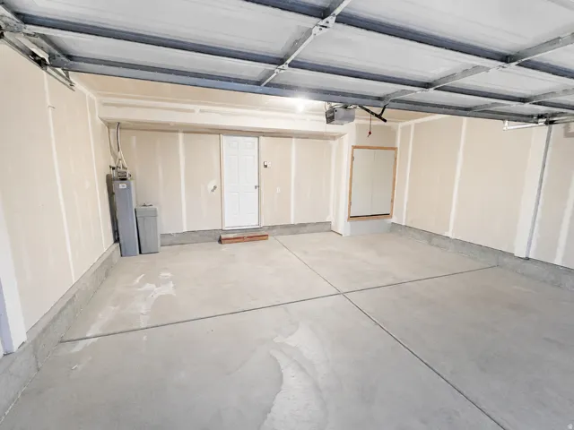Spacious garage featuring a finished concrete floor, exposed ceiling joists, and a side access door